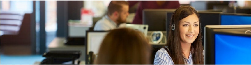 Smiling call center woman sitting down looking at a computer monitor.
