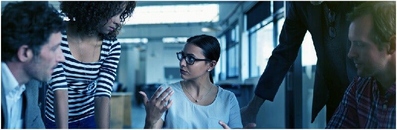 Woman wearing glasses in a meeting about customer feedback with four people.