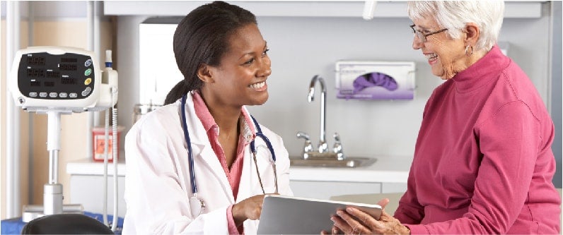 A doctor and patient are smiling at each other while viewing information on a tablet.