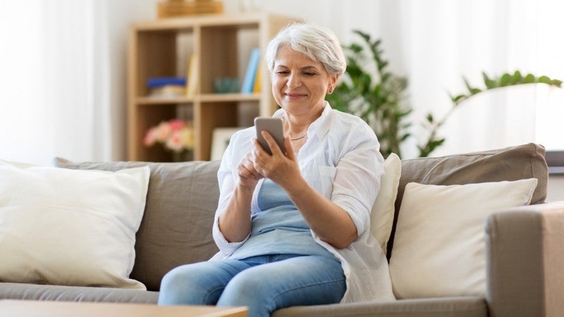 Elderly woman sitting on her couch using her phone.