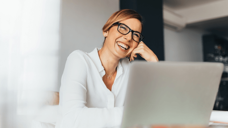 Woman smiling at her desk in front of her laptop.