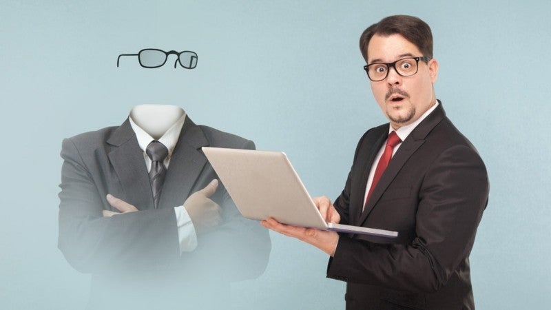Man in a business suit typing on his laptop computer with a ghost in the background.