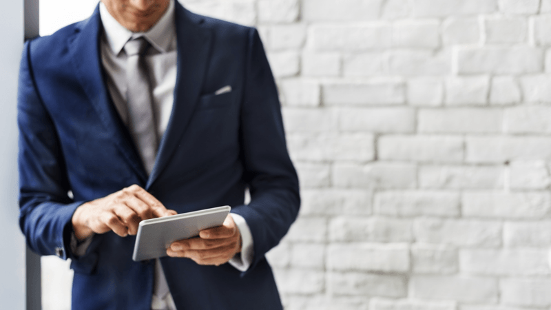 Man in a blue suit typing on his tablet.