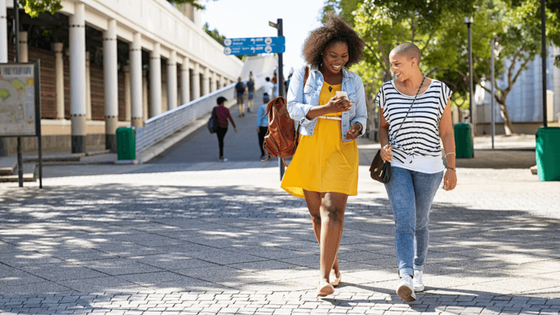 Two women walking while looking at a phone together.