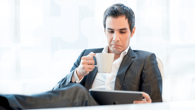 Man in a business suit drinking a cup of coffee while looking at a tablet.