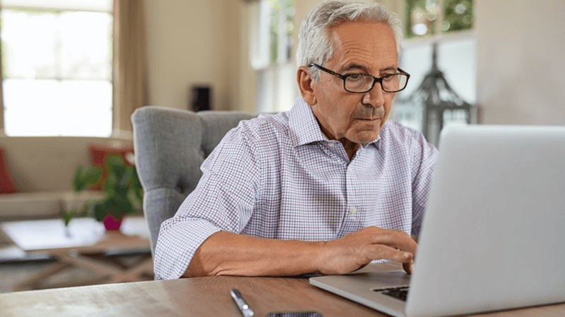 Older man typing on a laptop computer.