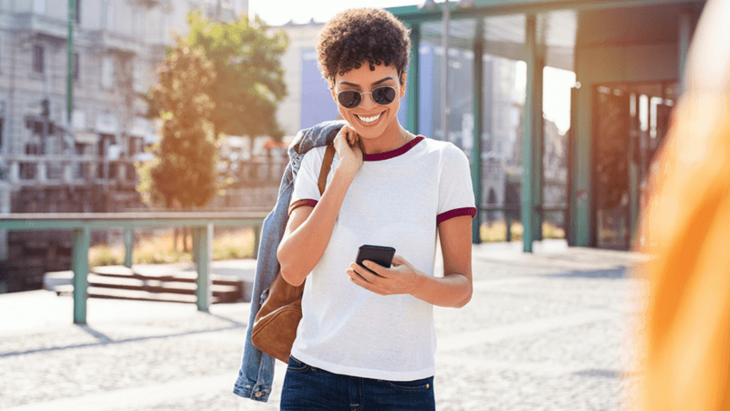 Smiling woman wearing sunglasses looking at her phone.