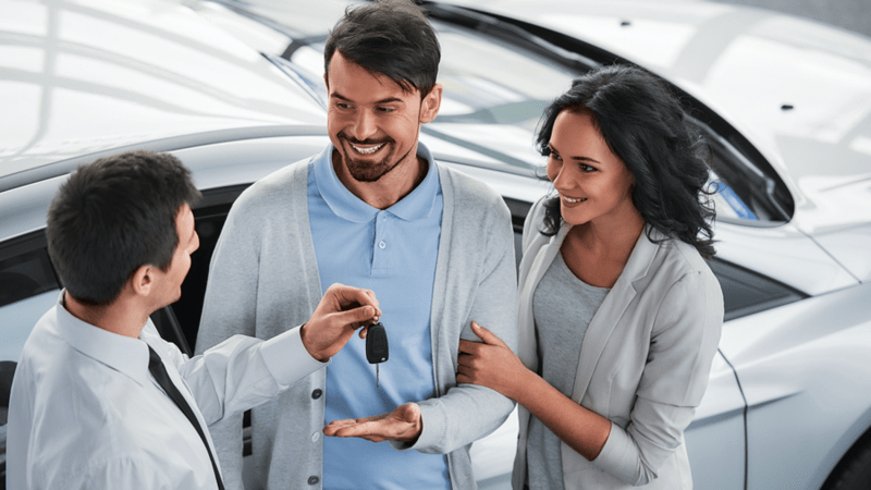 Car salesman handing keys to a smiling couple.