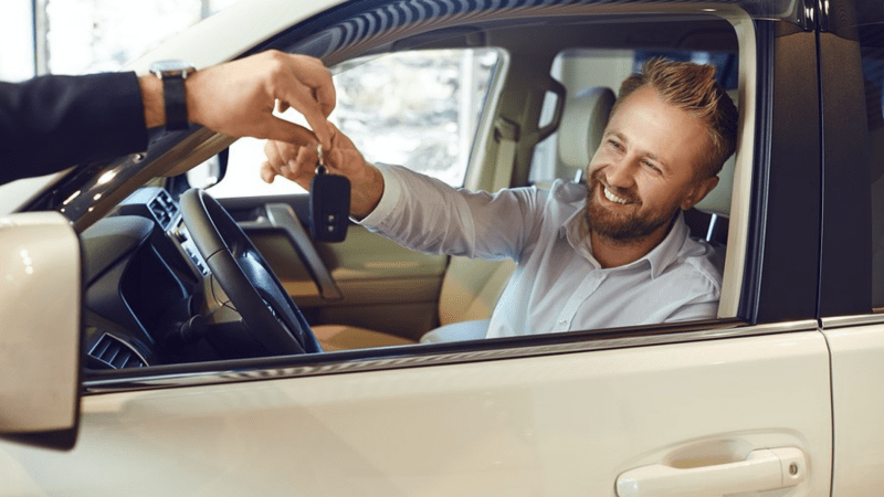 Man receiving a set of keys from a car salesman.