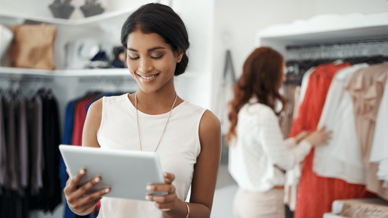Smiling woman looking at a tablet in a clothing shop.