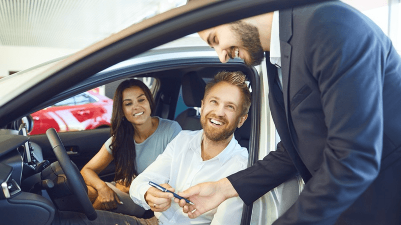 Car salesman handing keys to a happy new owner.