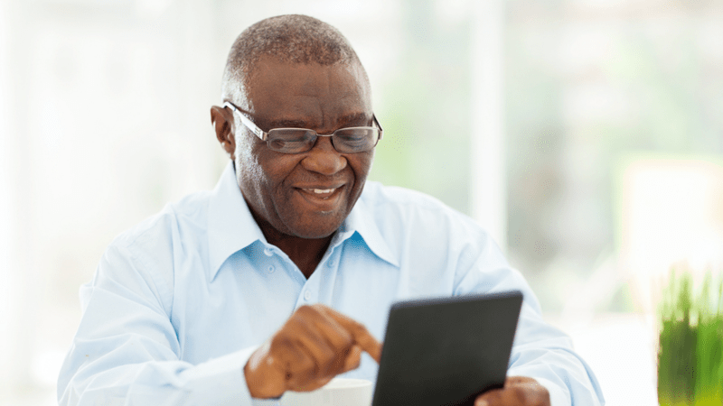 Smiling man wearing glasses while typing on a tablet.