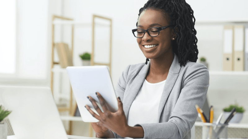 Smiling woman wearing glasses while looking at her tablet.