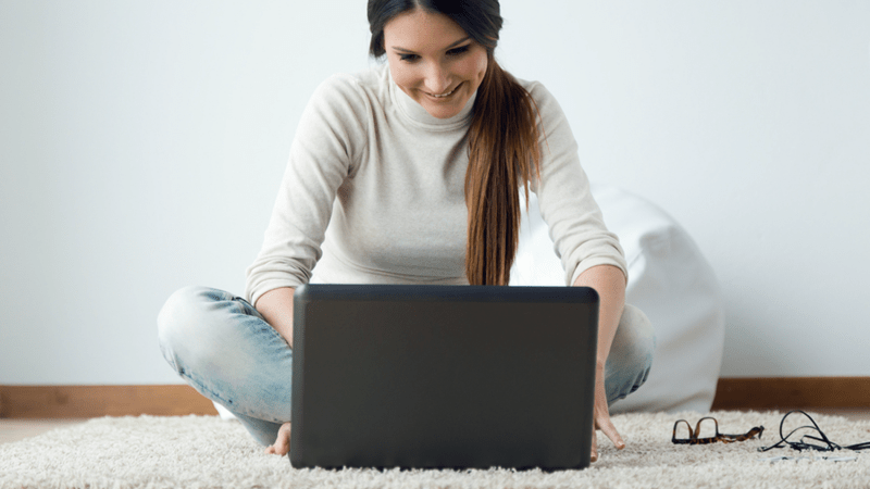 Woman sitting down on the floor looking at her laptop screen.