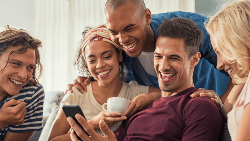 Group of people smiling and laughing while lookin at a phone.