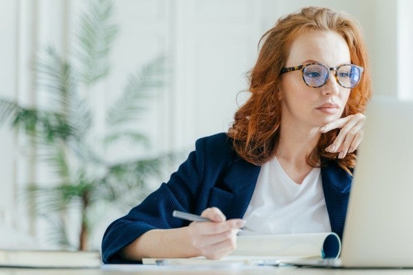 Woman looking at her laptop screen and taking notes. Woman looking at her laptop screen and taking notes.