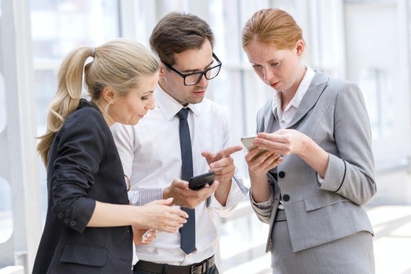 Three colleagues looking at information on a phone. Three colleagues looking at information on a phone.