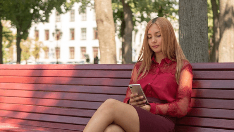 Woman sitting on a park bench looking at her phone.