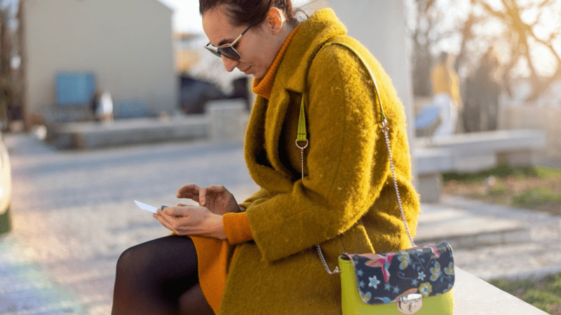 Woman sitting outside typing on her phone.