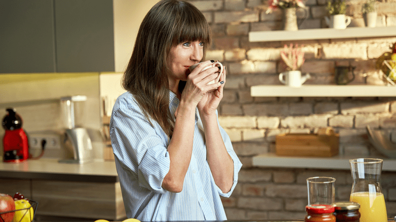 Smiling woman drinking a cup of coffee in her kitchen.